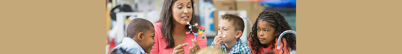 A Hispanic woman teaching a multi-ethnic group of elementary school students in science lab.